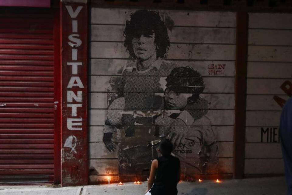Junge kniet vor Wandbild von Diego Maradona