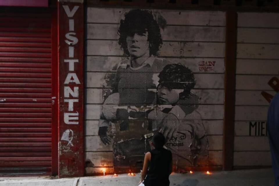 Junge kniet vor Wandbild von Diego Maradona Junge kniet vor Wandbild von Diego Maradona