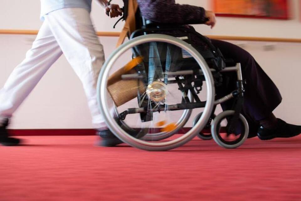 Ein Pfleger schiebt eine Frau in einem Rollstuhl