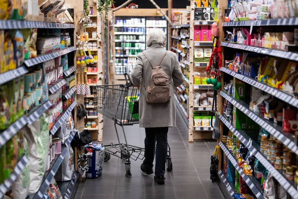 Eine Frau geht mit ihrem Einkaufswagen durch einen Supermarkt Eine Frau geht mit ihrem Einkaufswagen durch einen Supermarkt