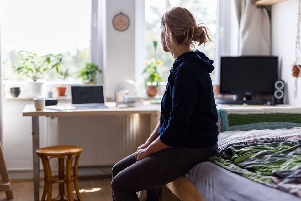 Eine Studentin sitzt auf dem Bett in ihrem WG-Zimmer