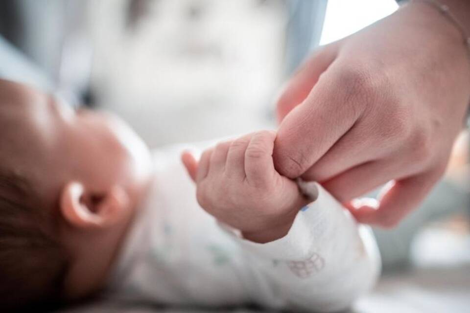 Ein Baby hält sich an der Hand einer Erwachsenen fest