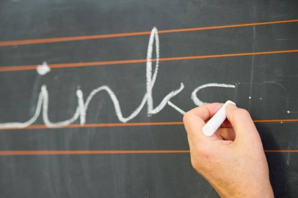 Eine linke Hand schreibt an der Tafel Eine linke Hand schreibt an der Tafel